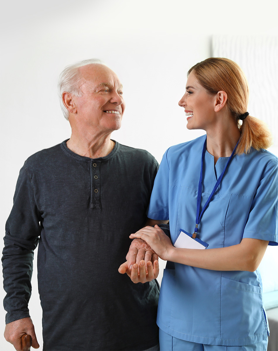 Nurse and male patient walking arm in arm down a hallway.