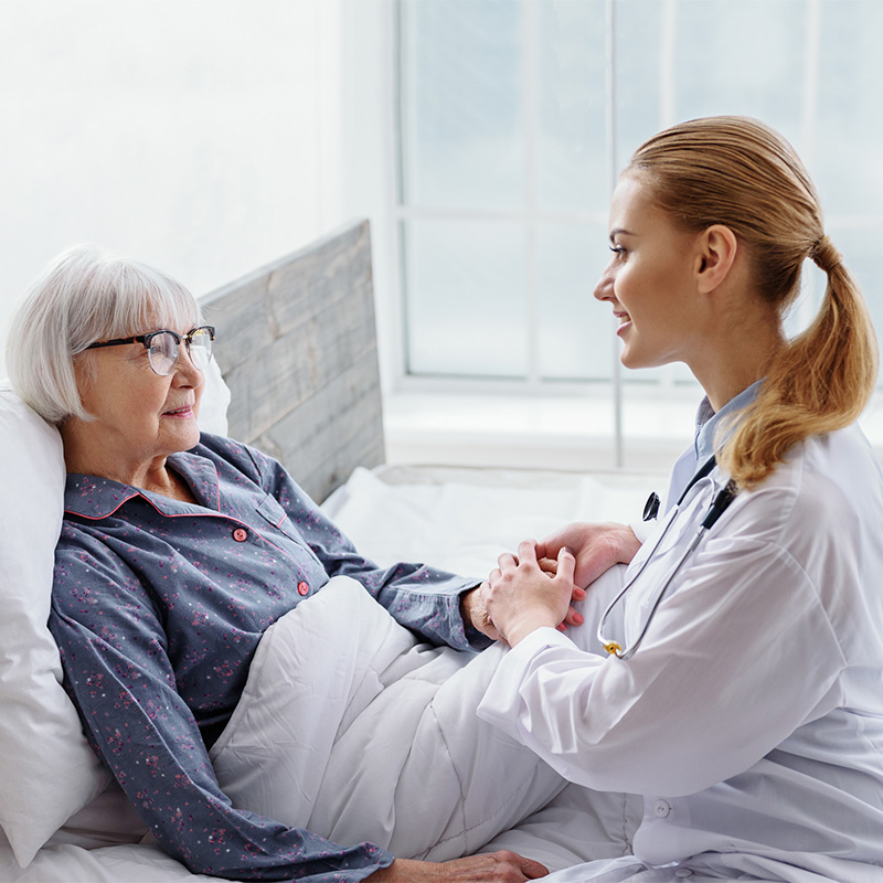 Doctor seated at a resident's bedside speaking and holder her hand.